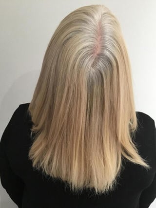 Foto de antes: vista trasera de una mujer con cabello rubio de media melena con mechas negras antes de la coloración.