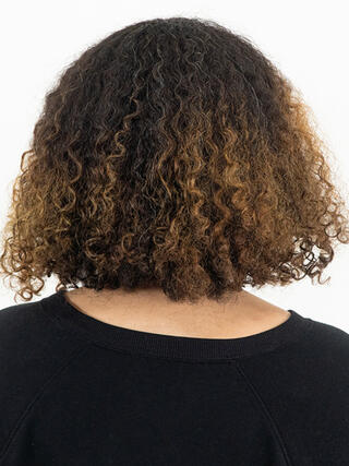 Foto de antes: vista trasera de una mujer con cabello negro corto y rizado con las raíces crecidas antes de la coloración.